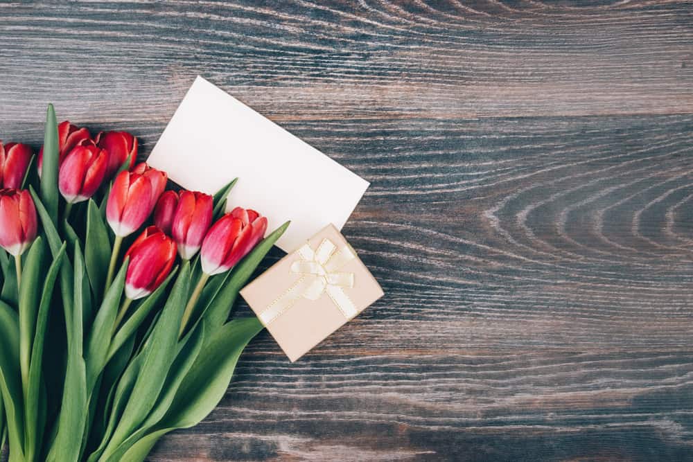 un bouquet de tulipes, un cadeau et une carte de voeux se tiennent sur la table