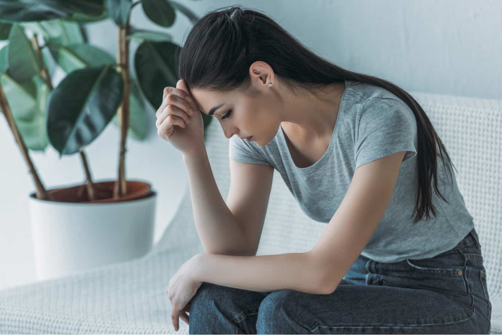 une femme aux longs cheveux noirs est assise sur le canapé, la tête baissée