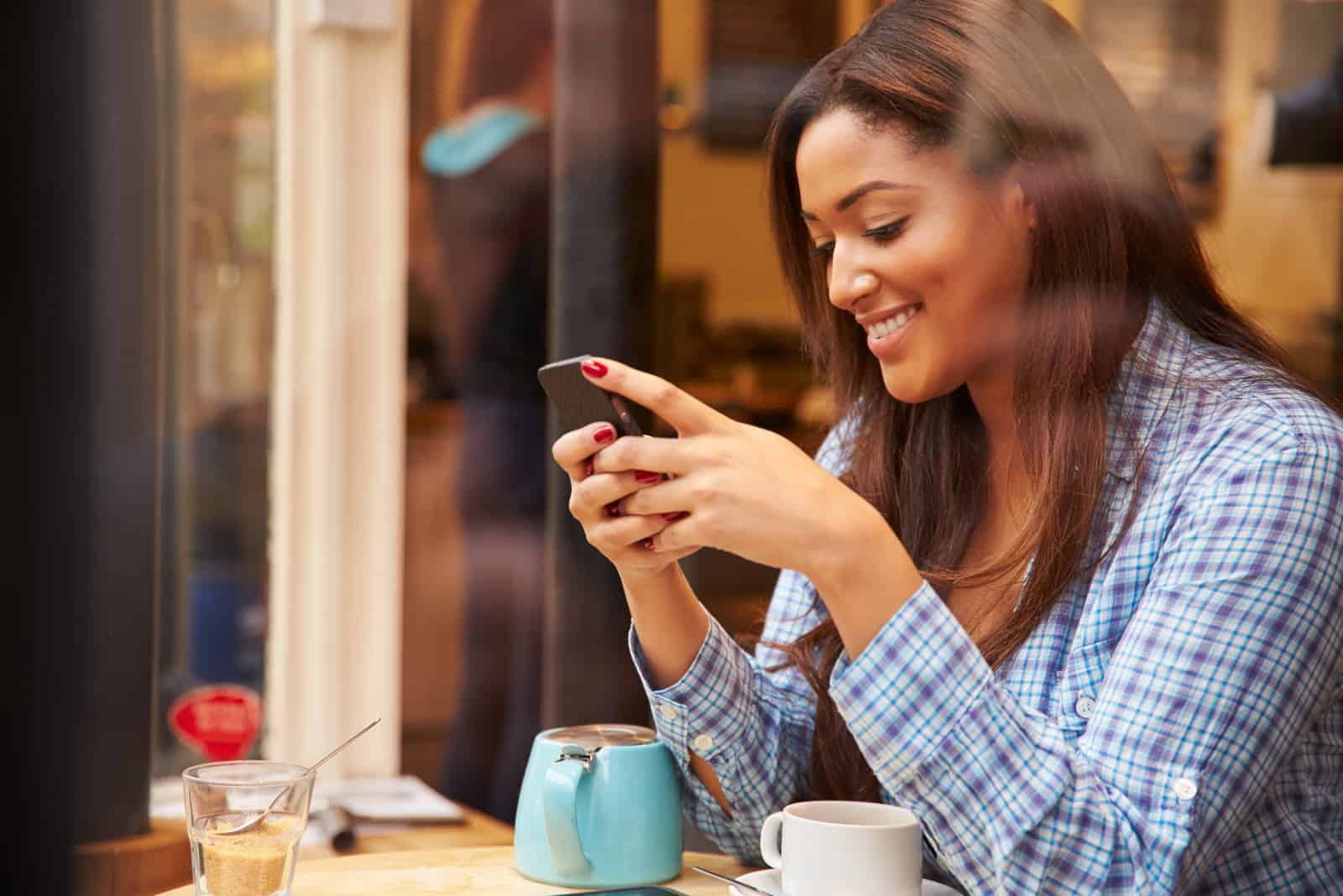 une femme souriante aux cheveux bruns est assise à une table et des boutons sur le téléphone