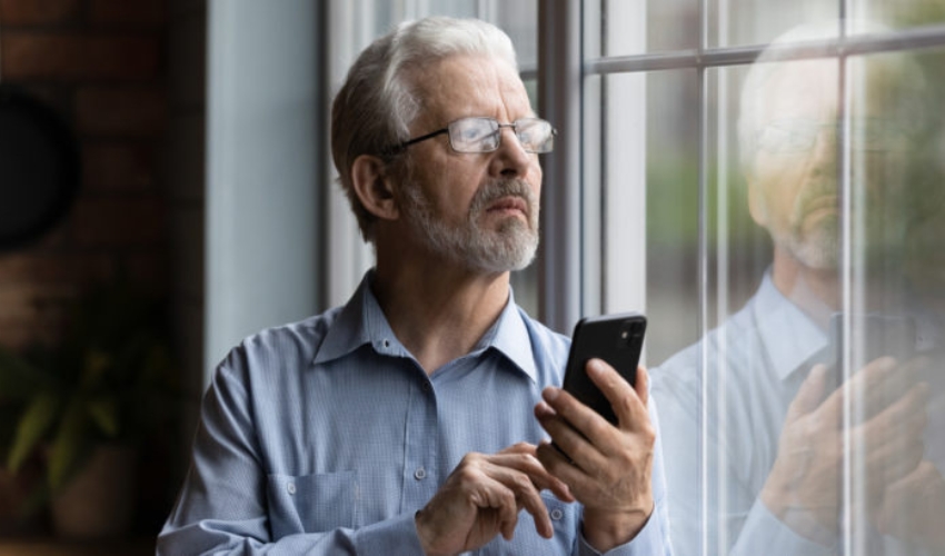 homme plus age tenant son telephone tout en regardant par la fenetre
